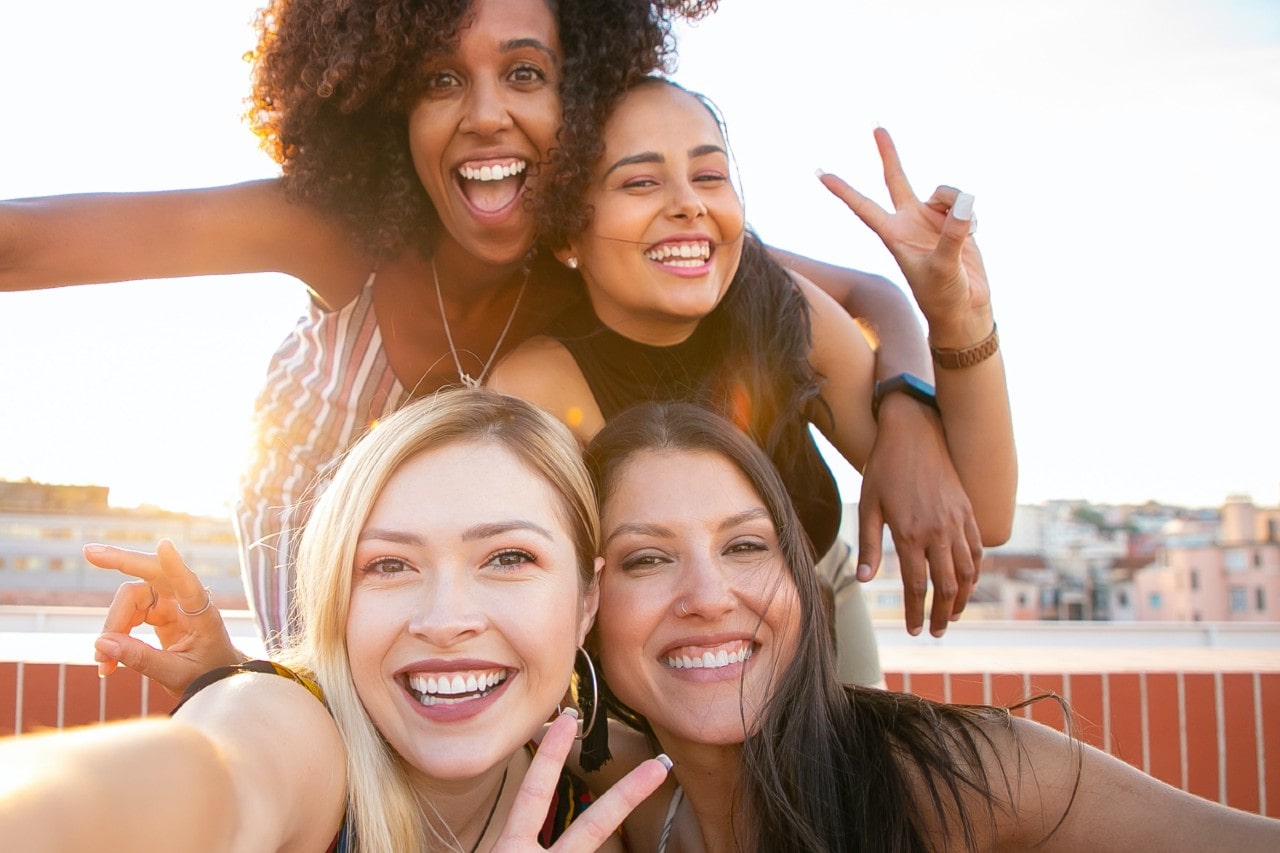 Four best friends gather for a selfie while showing off their jewelry on a terrace overlooking the city during sunrise