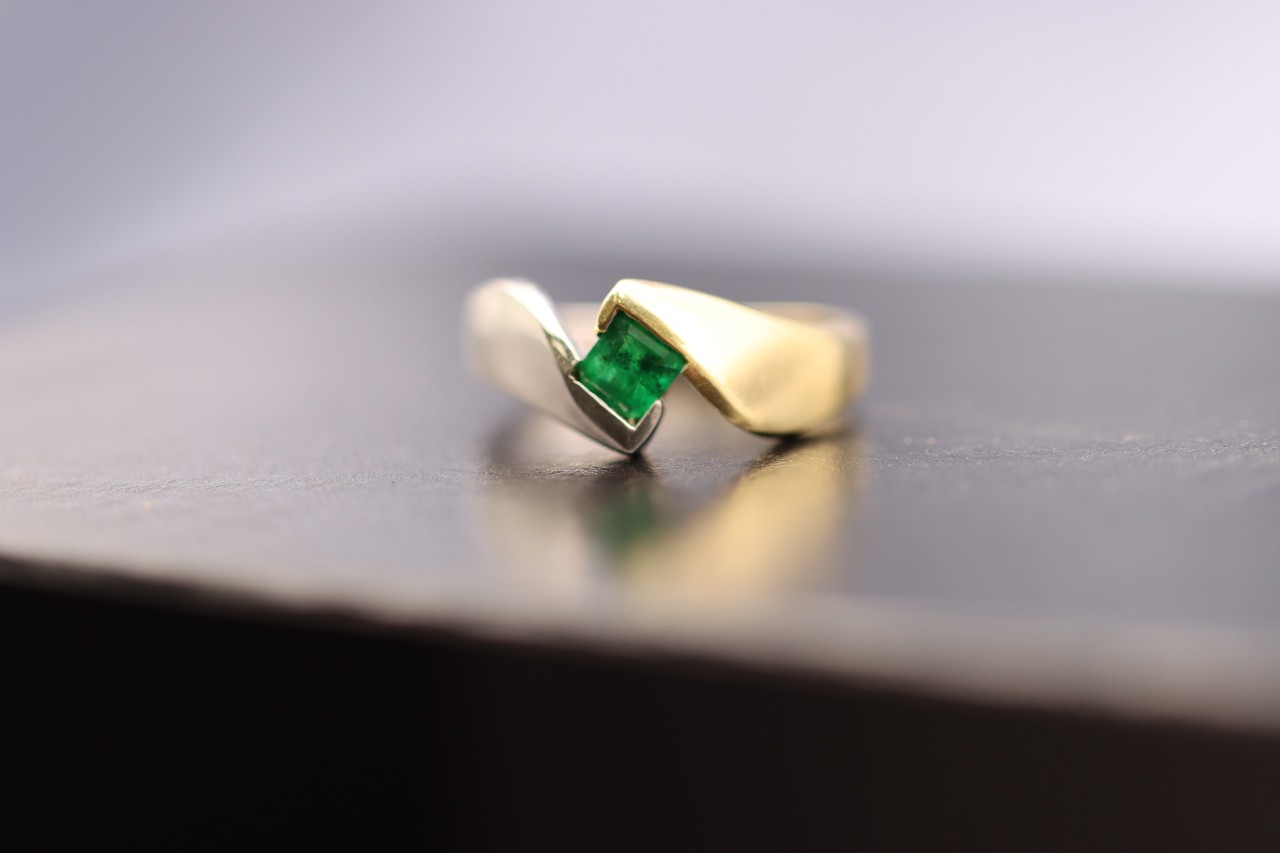 A solitaire emerald princess cut stone bezel set in a mixed metal ring