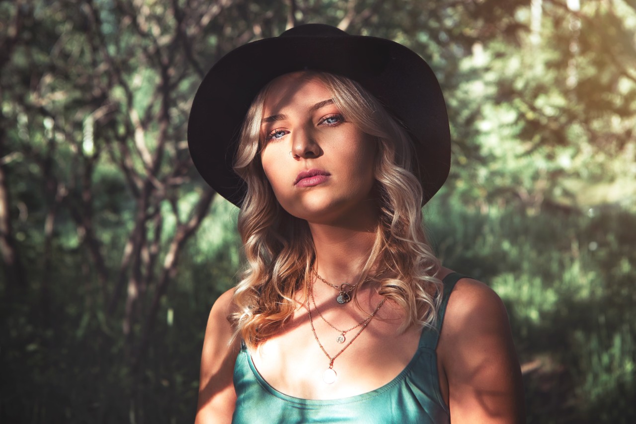 Woman wearing a sun hat, a green shirt, and three glamorous necklaces