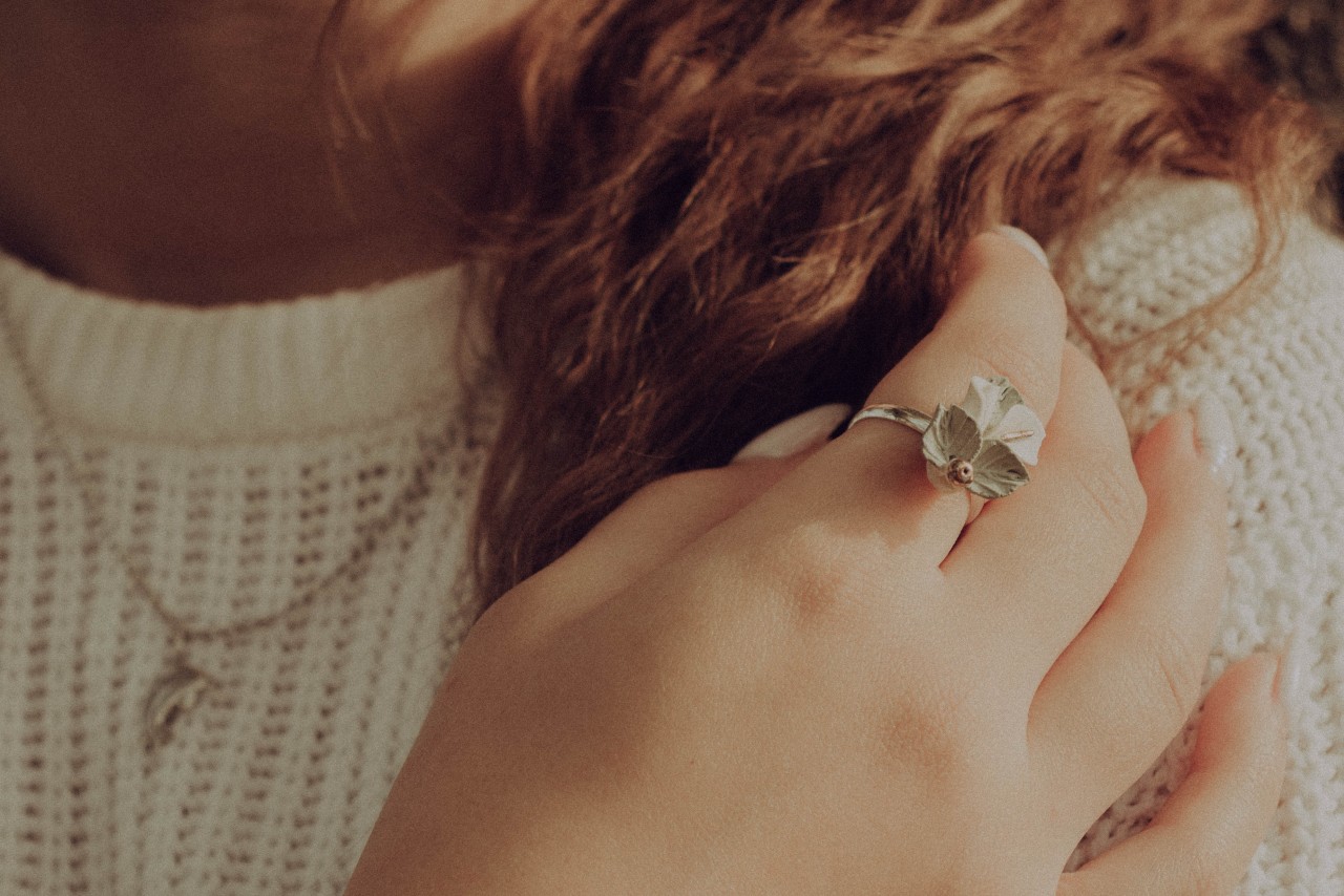 A woman touches her hair while wearing a sweater, a necklace, and a fashion ring