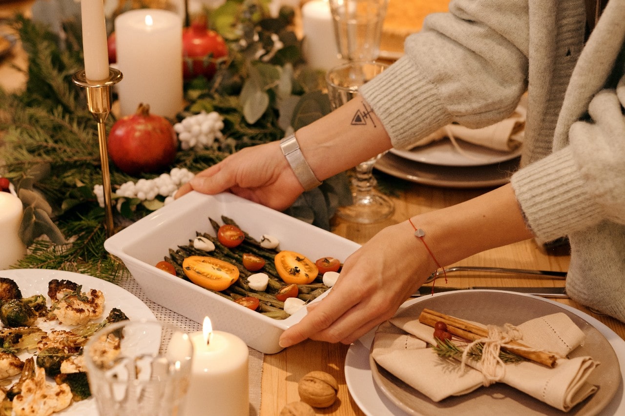 A woman wearing bracelets sits down a casserole dish at a Thanksgiving dinner