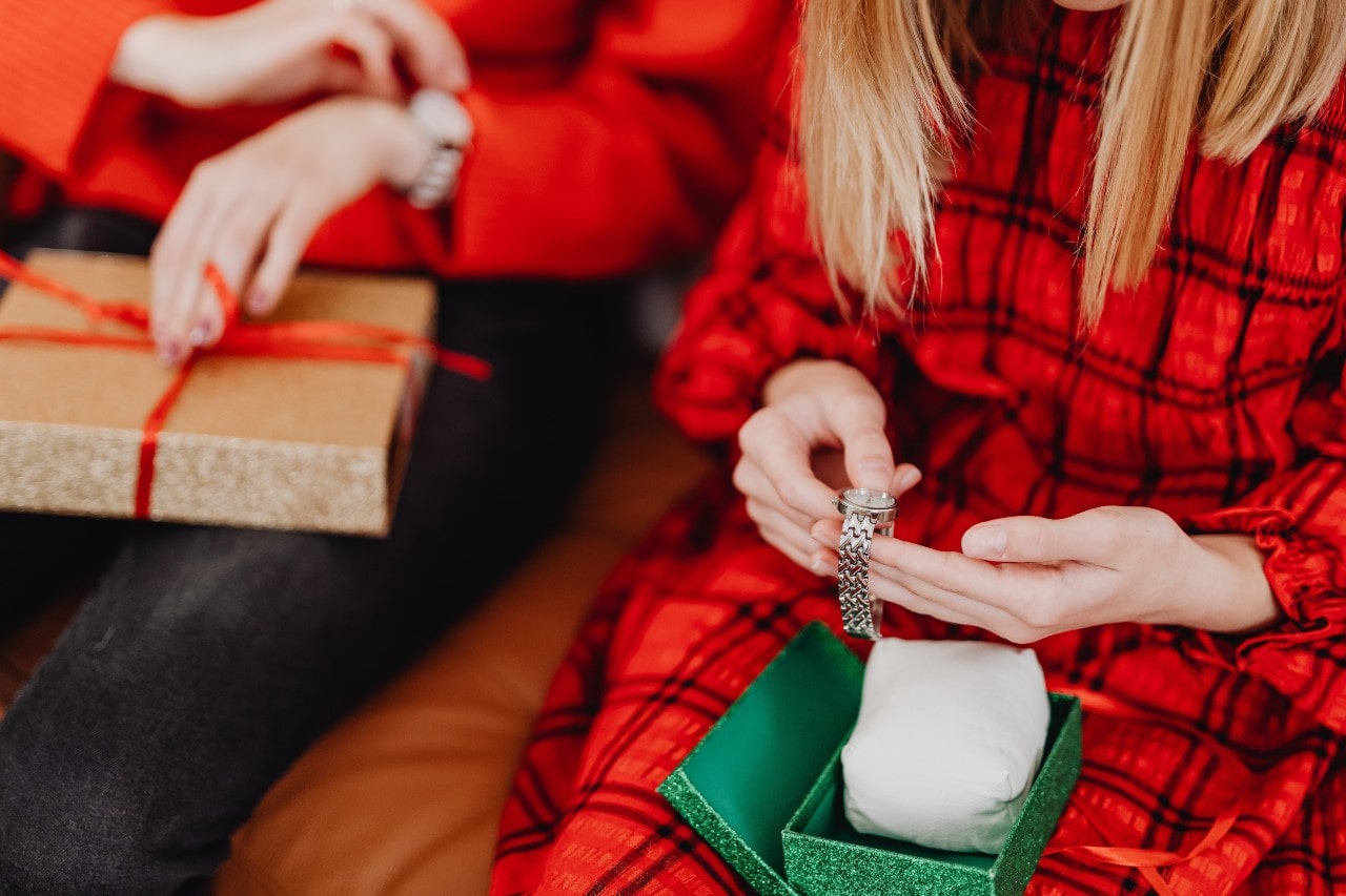 people dressed in festive clothing, one of which is opening a gift box containing a silver watch