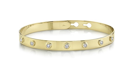 a yellow gold bangle bracelet featuring bezel set diamonds