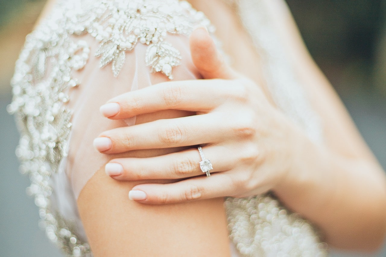 a bride’s hand resting on her arm, wearing a simple white gold engagement ring