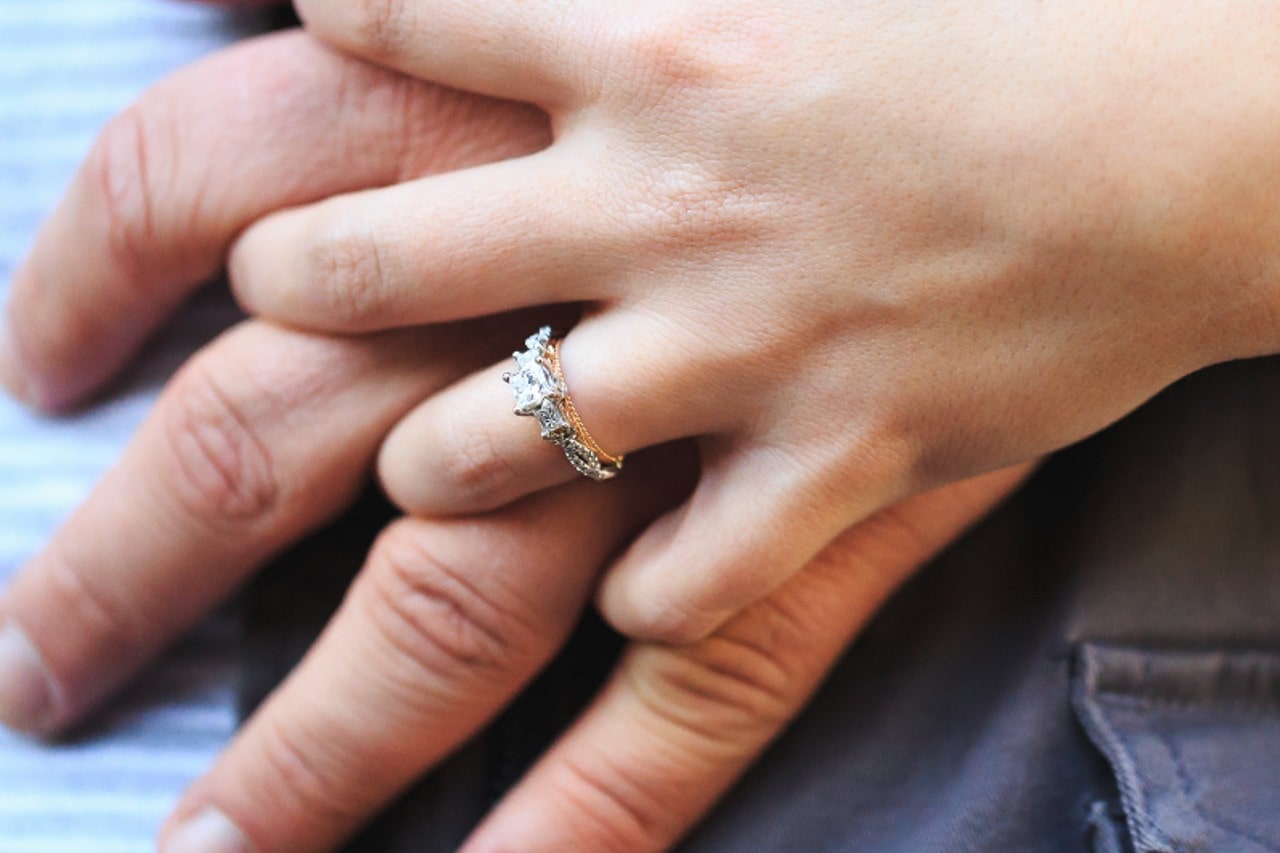 a close-up of a couple holding hands, with emphasis on the mixed metal engagement ring adorning the woman’s finger