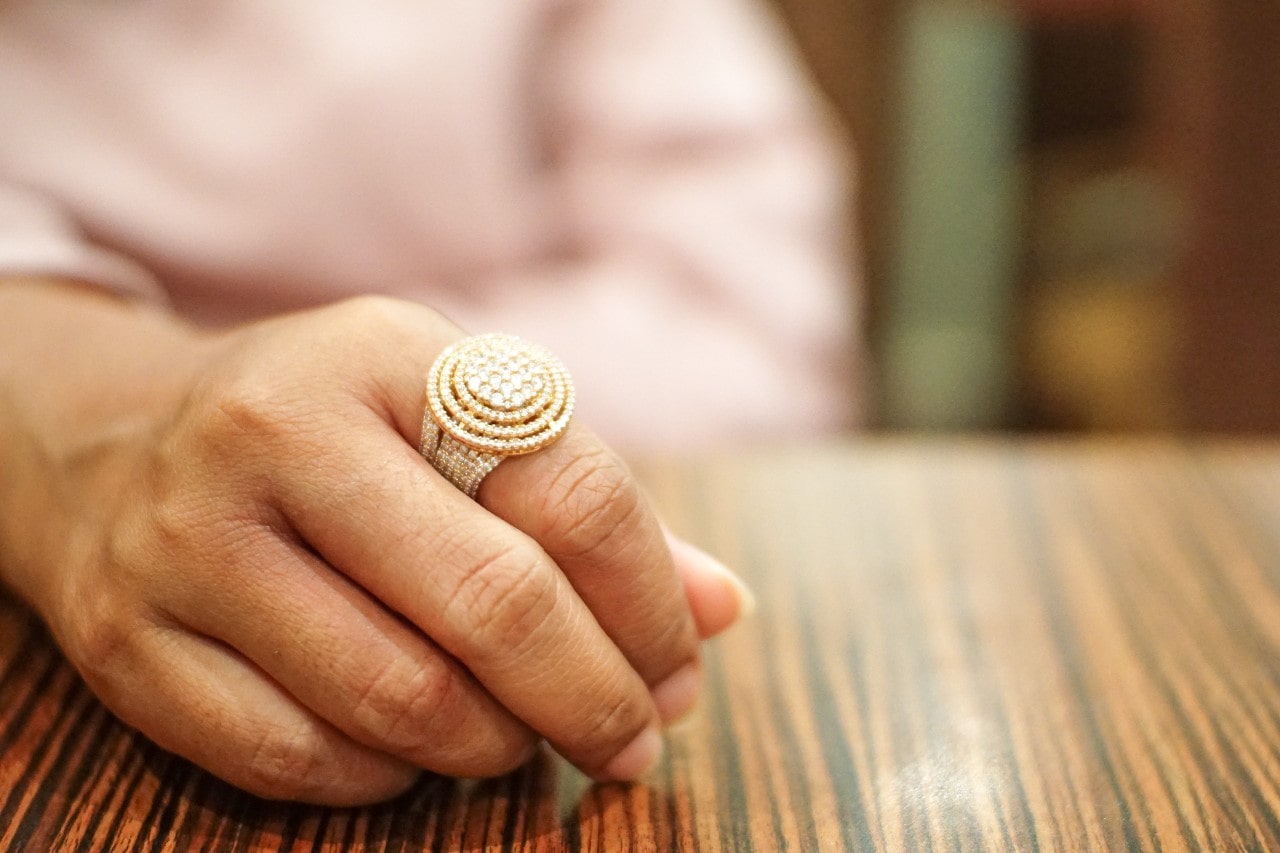 A close-up of a person’s hand, wearing an ornate diamond and gold ring.