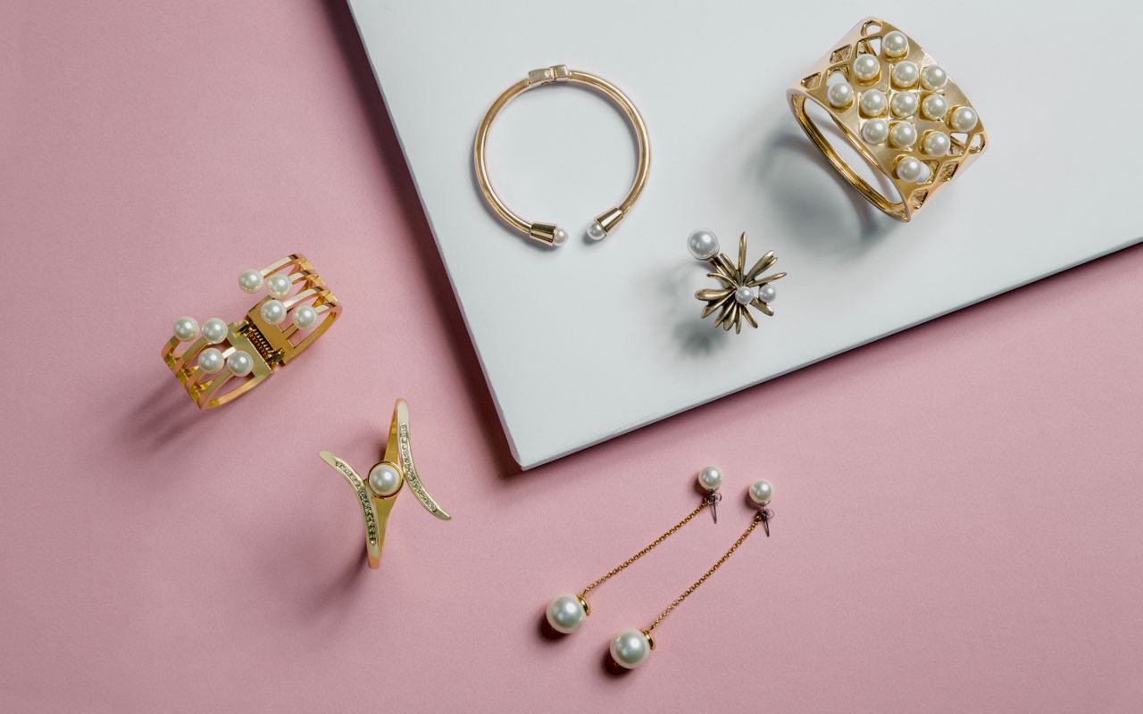 A selection of gold and pearl jewelry on a delicate pink and white surface.