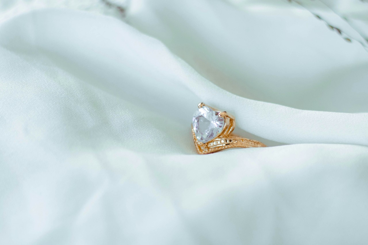 a rose gold engagement ring with a heart shaped center stone on a white sheet