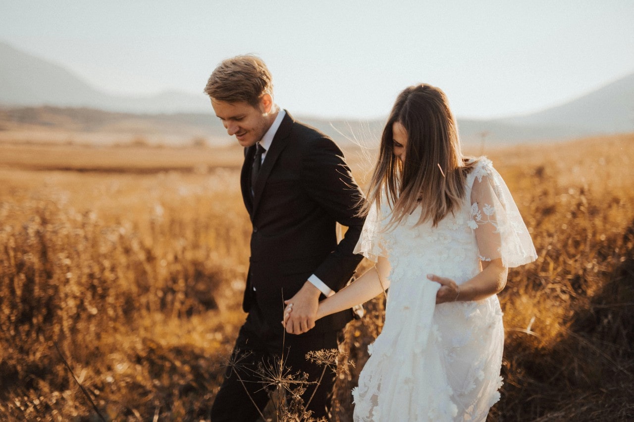 a bride and groom walking through a field in the fall