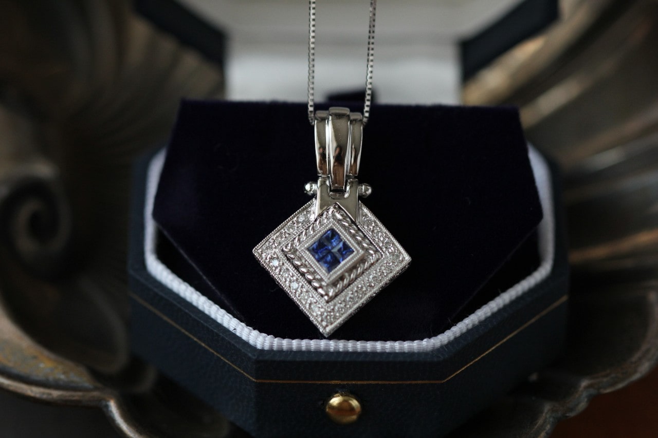 A close-up of an opulent sapphire pendant necklace displayed in-box.