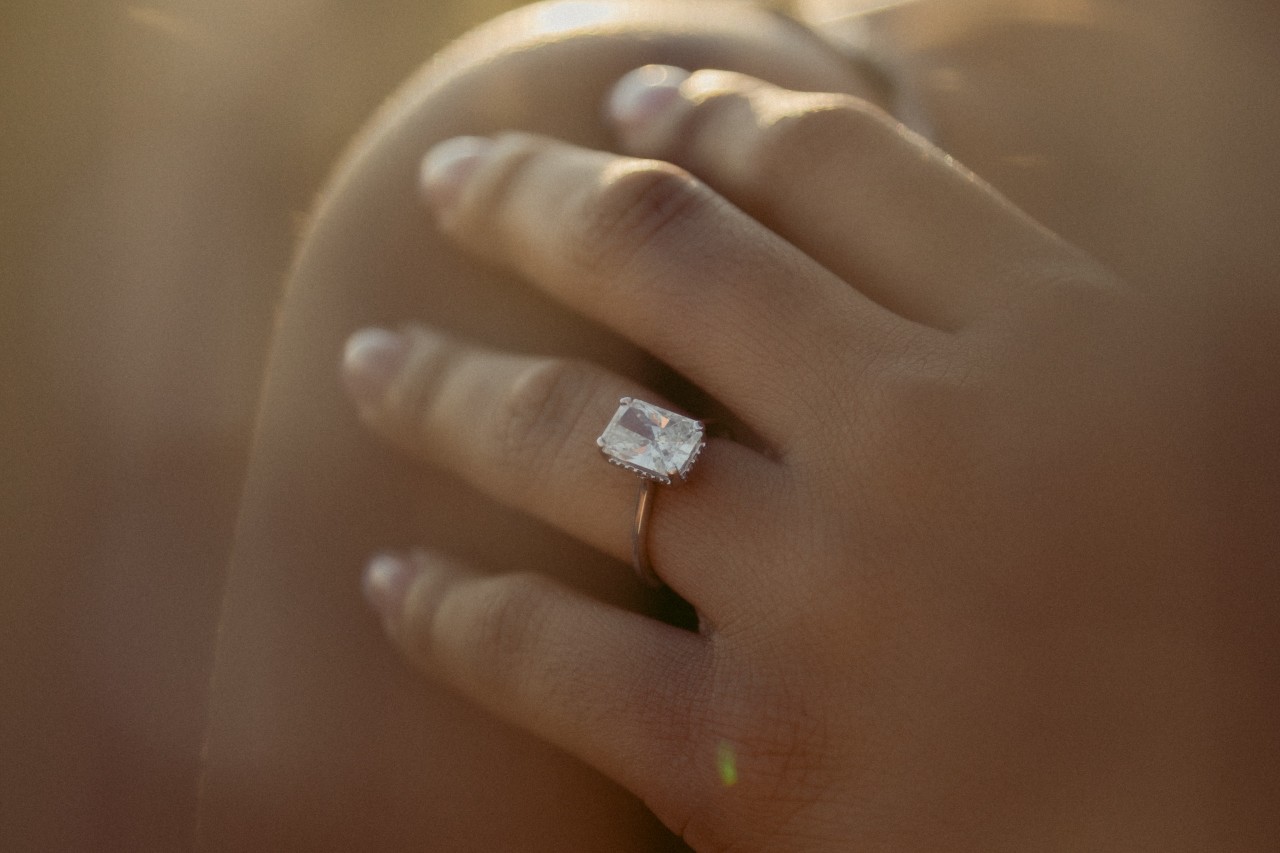 A close-up of a woman’s hands, adorned in a simple yet elegant engagement ring.