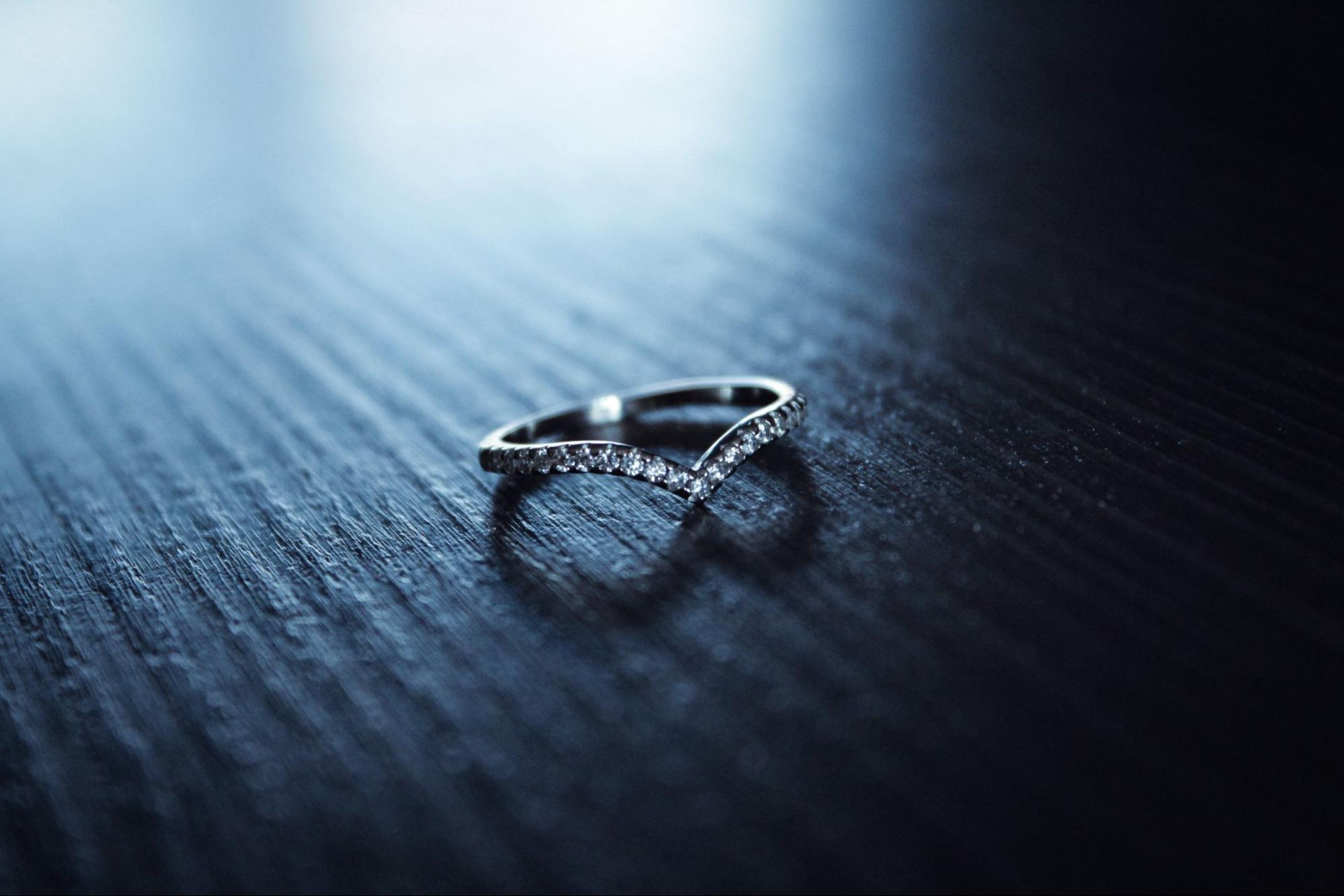 A close-up of a curved diamond wedding band sitting on a dark wooden surface.