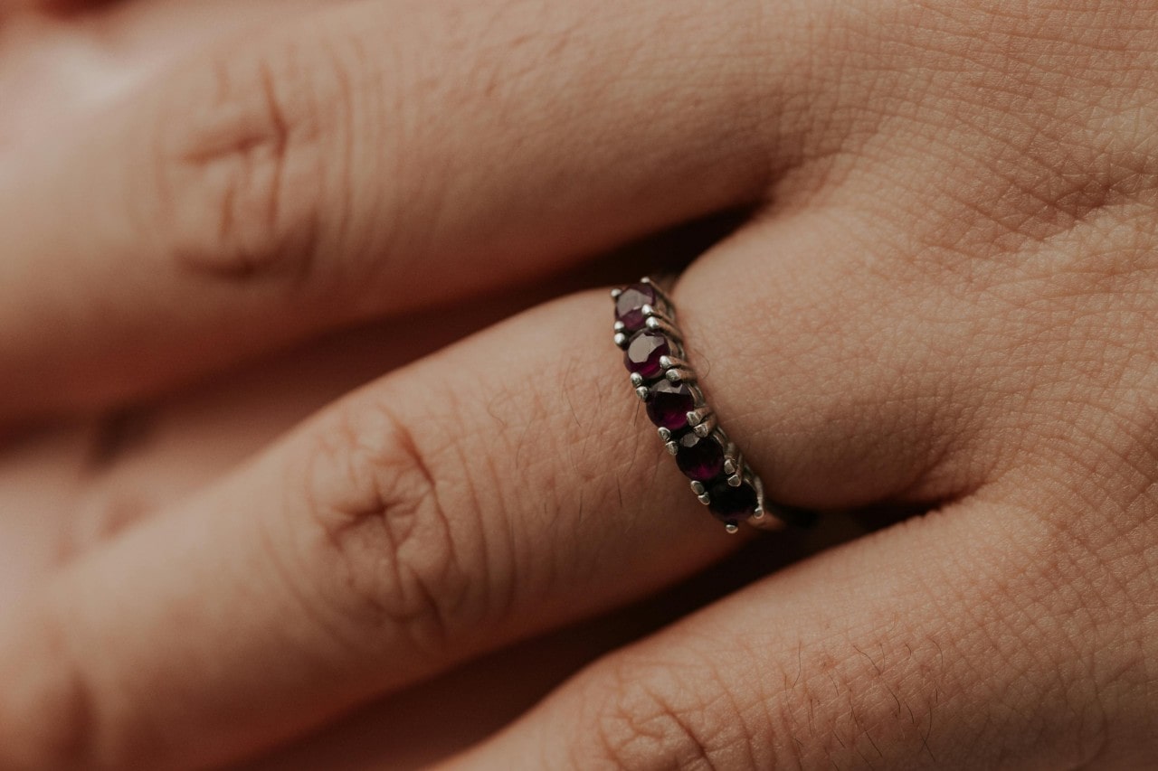 A close up of a white gold wedding band with round cut rubies on a hand.