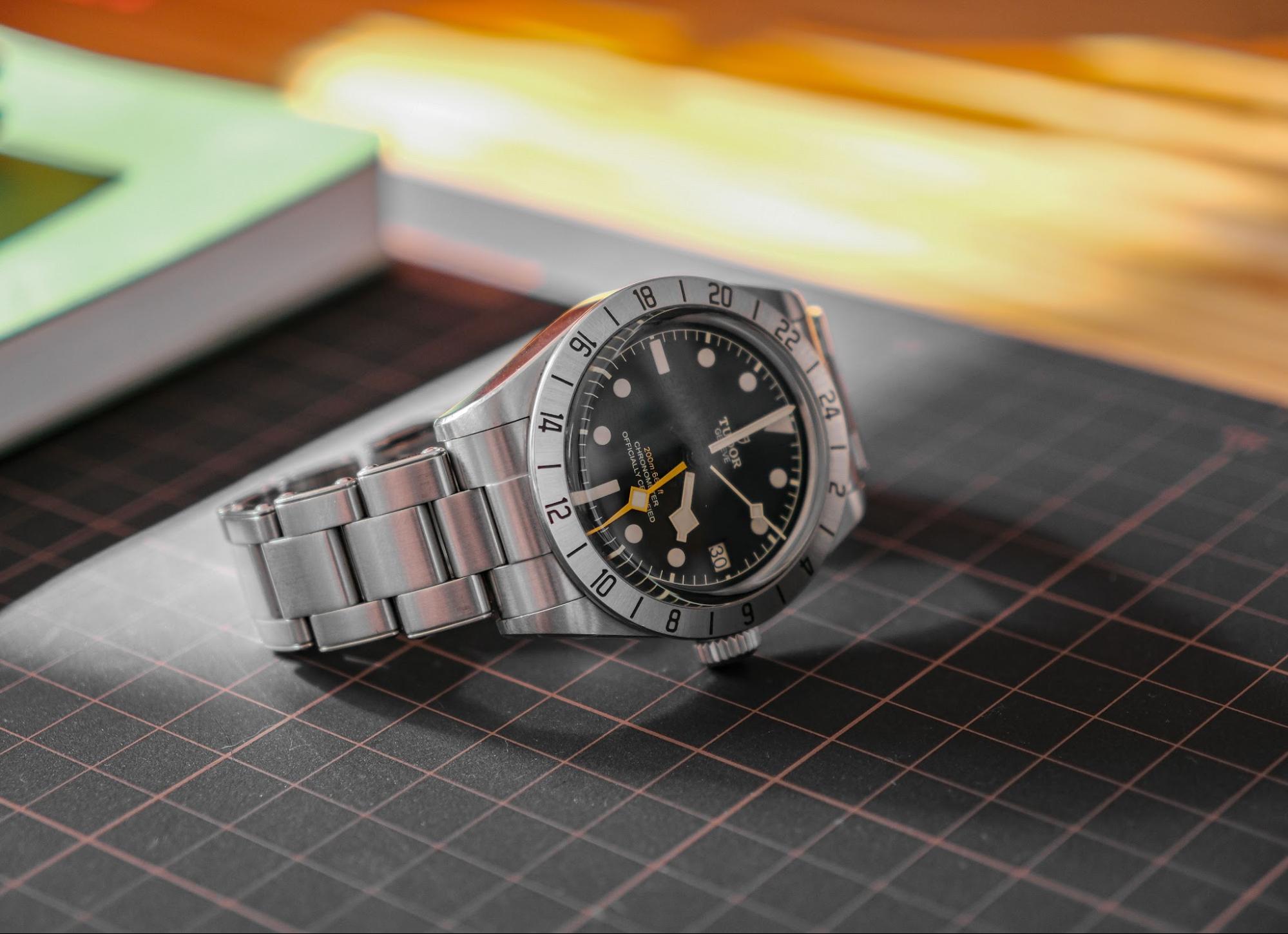 A close-up shot of a stainless steel Tudor Black Bay Pro GMT watch resting on a black grid mat.