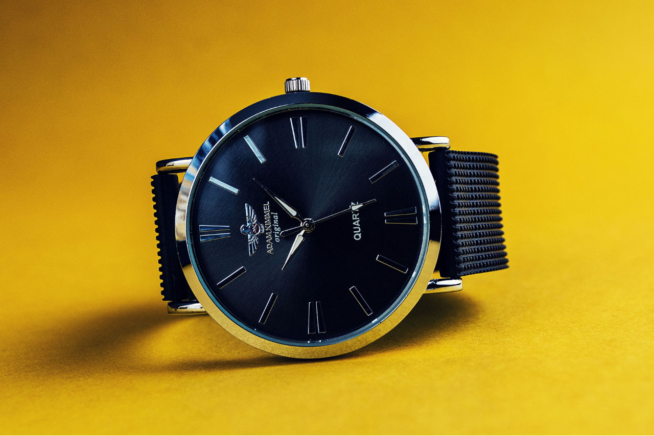 A black Adam Kimmel quartz watch on a vibrant yellow background.