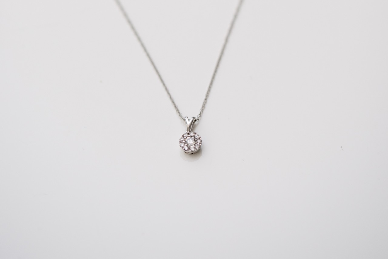 A delicate silver necklace with a round diamond pendant, elegantly displayed against a plain white background