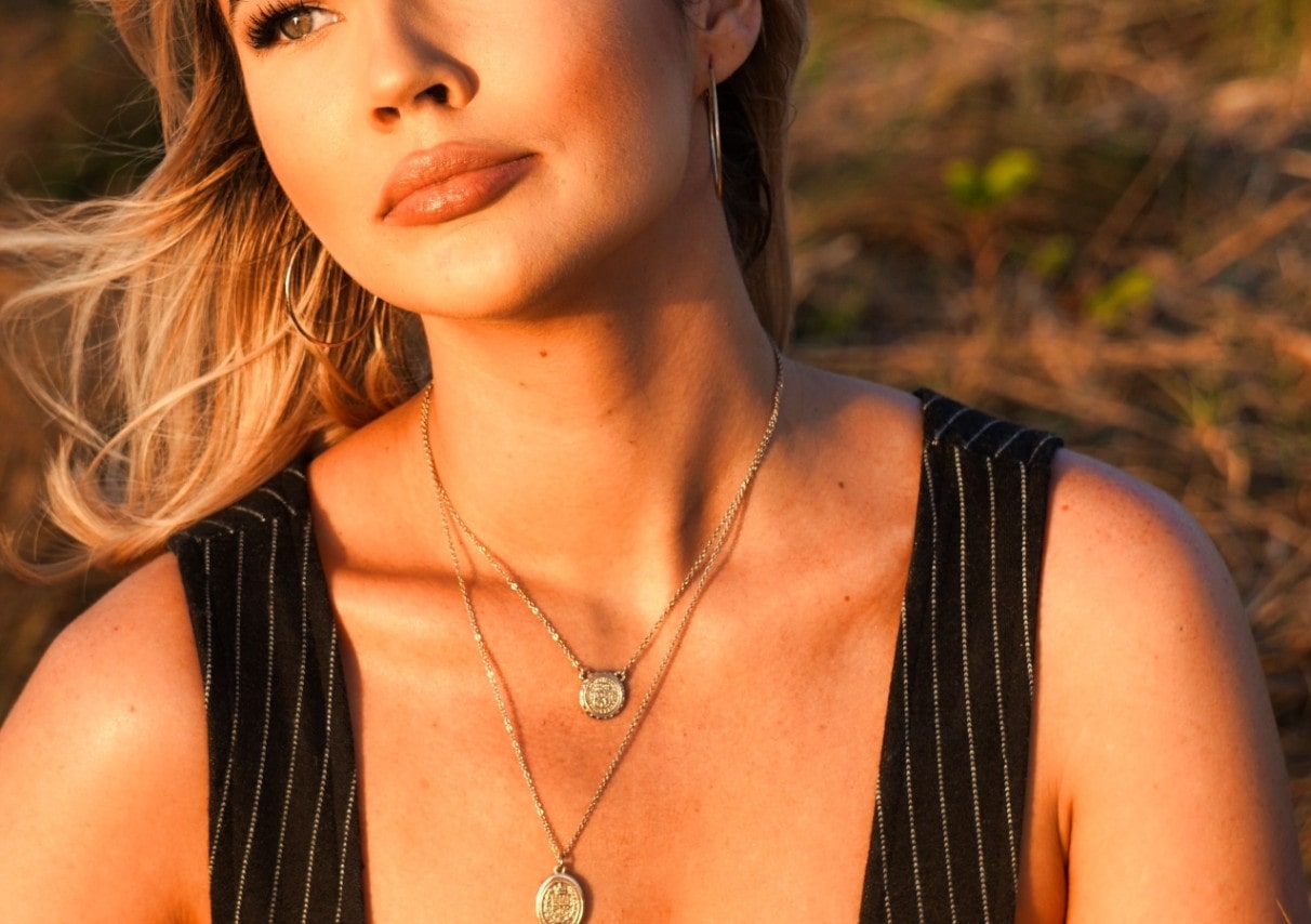 A woman wearing layered gold necklaces with coin pendants, accentuating her neckline in warm sunlight