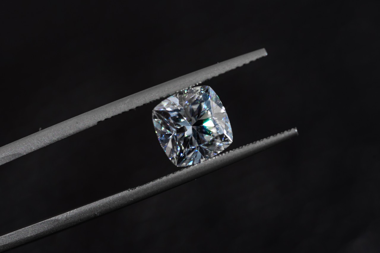 A cushion diamond being held between jeweler tweezers