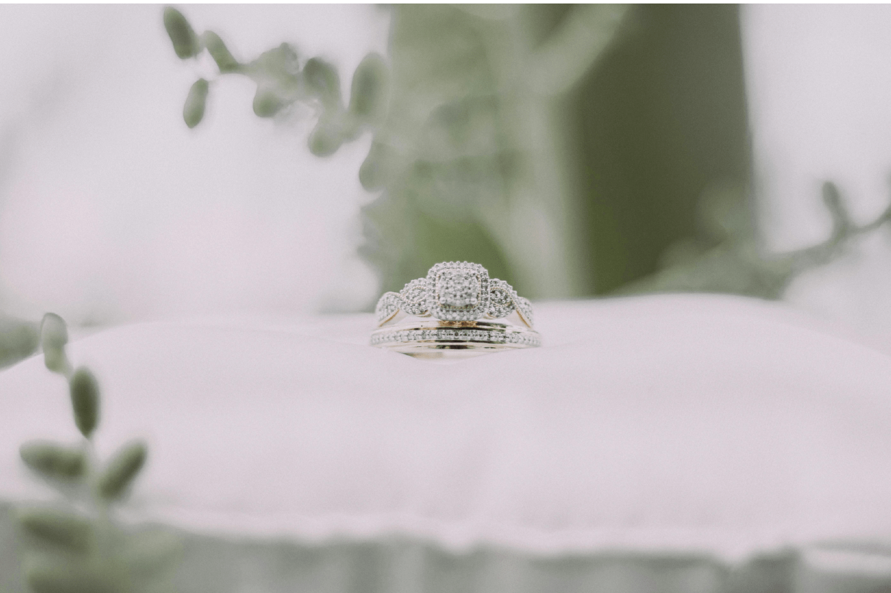 A white gold diamond engagement ring and wedding band sitting on a white pillow.