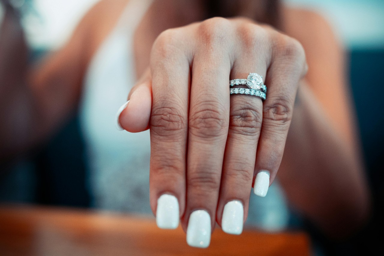 A woman’s outstretched hand, adorned with a diamond engagement ring and wedding band.