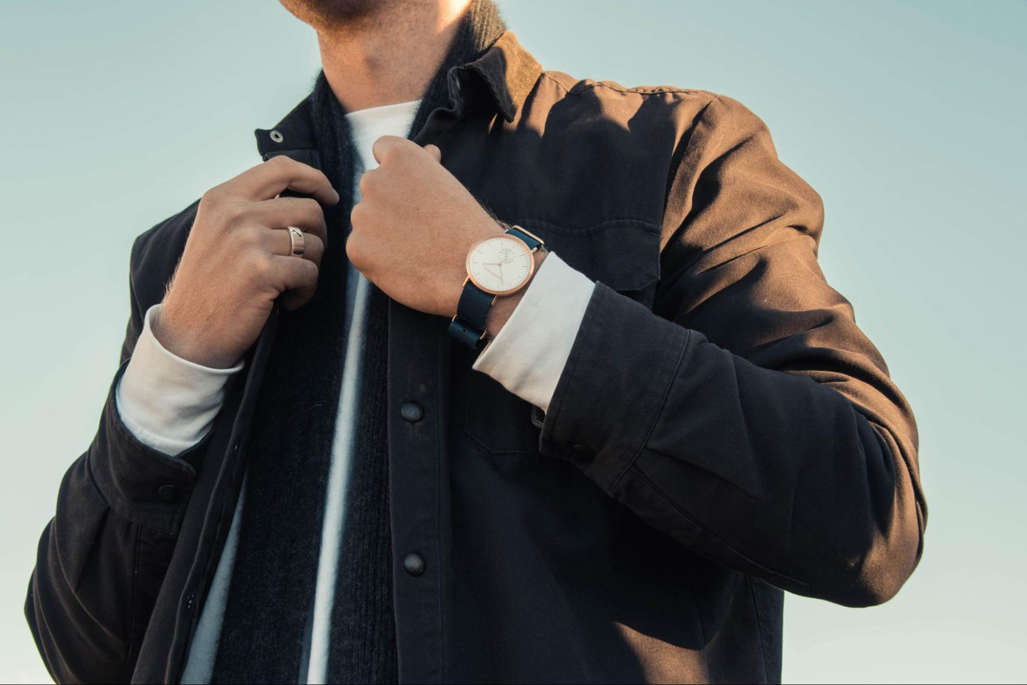 A man in a black coat and sweater wearing a luxury watch