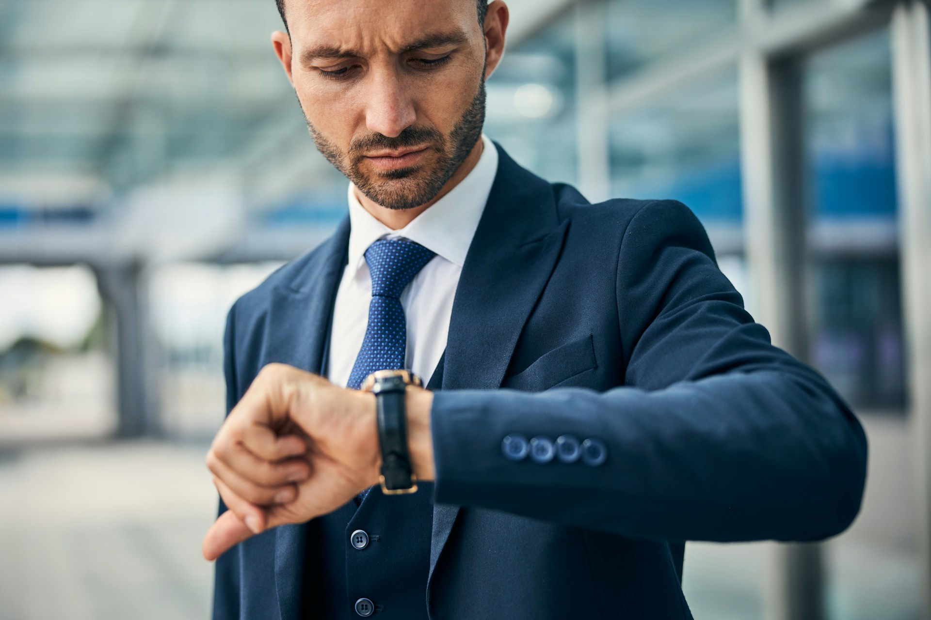 A man in a navy blue suit checking his match watch