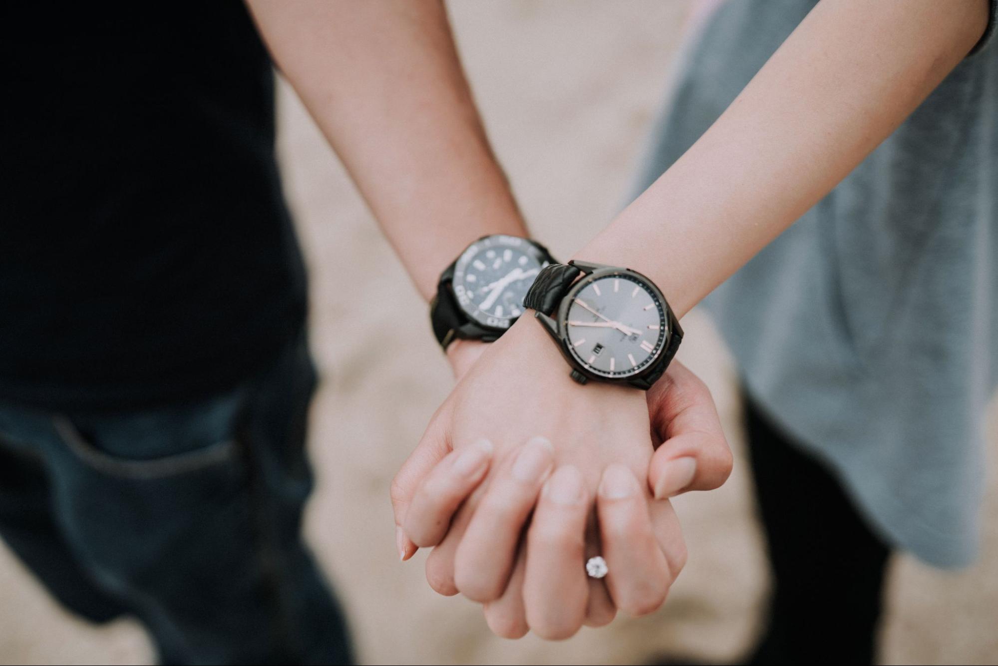 A couple holding hands and wearing match black timepieces