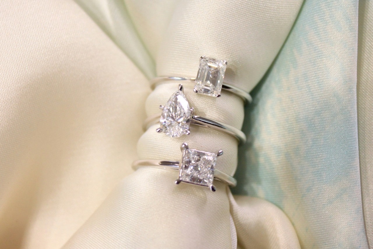 three diamond engagement rings with a cloth threaded through