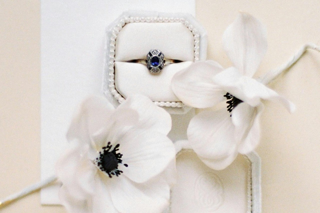 a trendy engagement ring in a white box next to white flowers